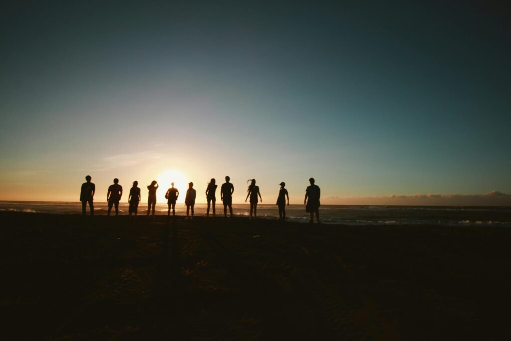 pexels photo 1000444 1000444 A group of friends standing on a beach, silhouetted against a vibrant sunset over the ocean.